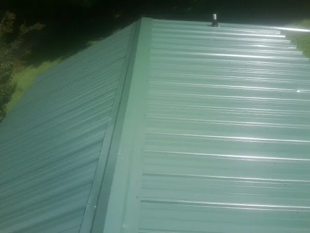 New green metal panels meeting at the ridge of a roof — Flat Roof Repair work by our crew in Carrollton
