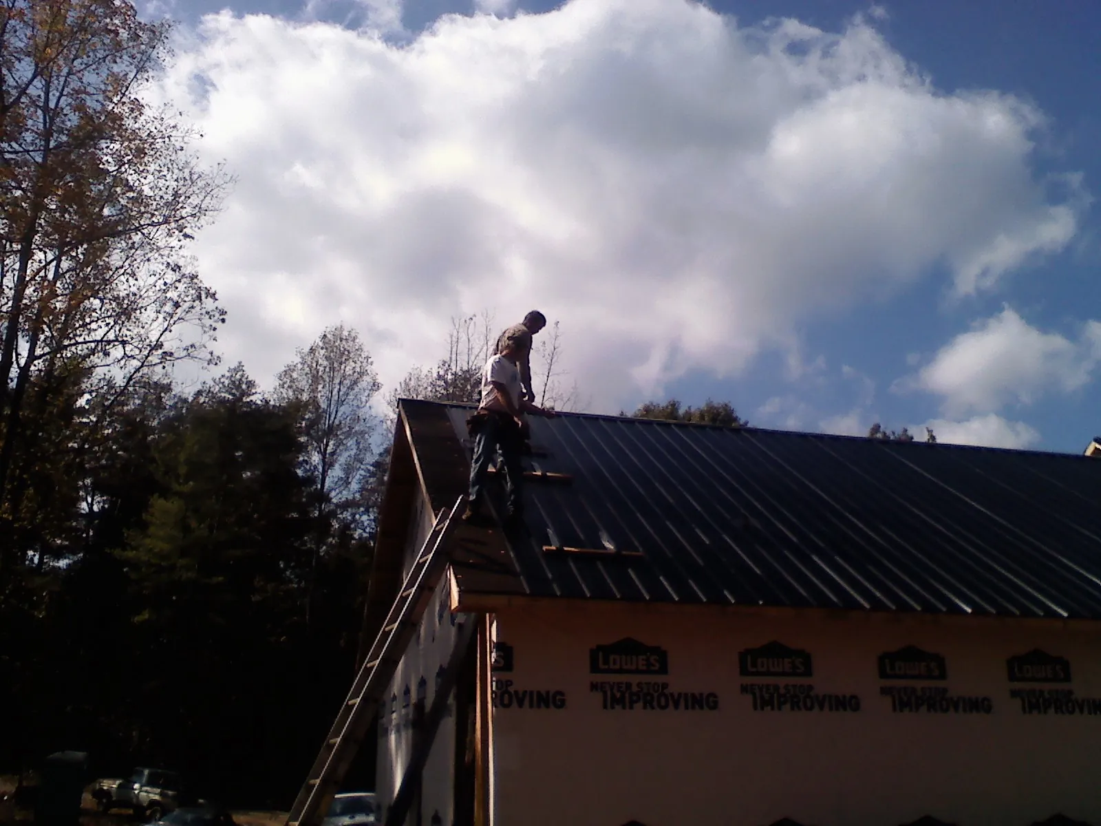 Roofer fastening dark metal panels high against a cloudy sky, from a Roof Inspection job in Carrollton