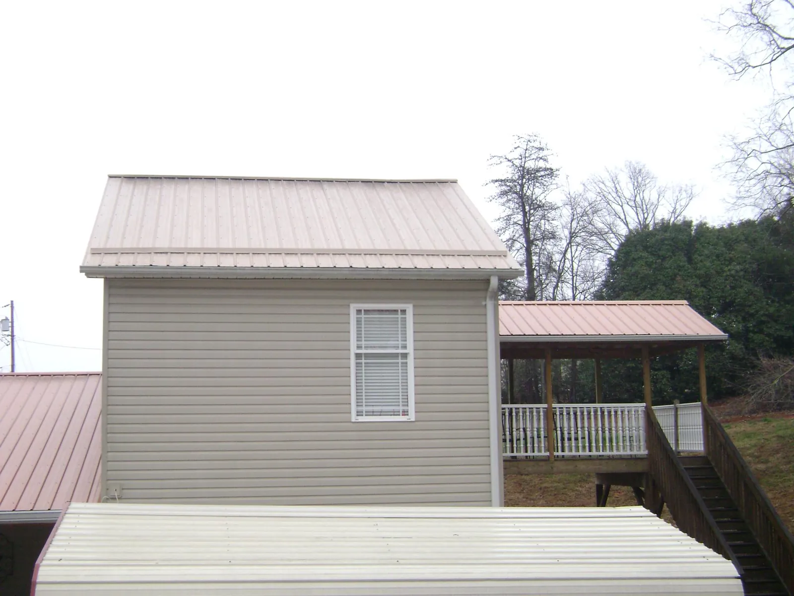Tan metal roofs on a two story addition and attached porch, from a Roof Replacement job in Carrollton